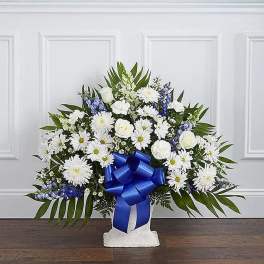 White and blue floral arrangement in a white vase with a blue ribbon