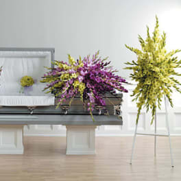 Sympathy floral set with purple and yellow sprays and a casket spray arranged around an open casket.