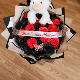 Plush cow sitting on a bouquet of red and black roses