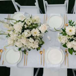 White floral centerpieces on a set dining table with gold flatware