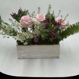 Pink roses and purple flowers arranged in a rectangular wooden box