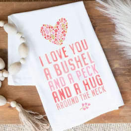 White decorative sign with pink floral heart and text on a wooden surface