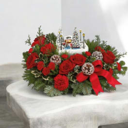 Red roses and pine arranged around a small winter village centerpiece