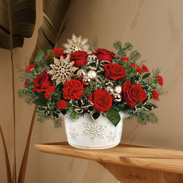 Red roses in a white snowflake-decorated vase with holiday accents