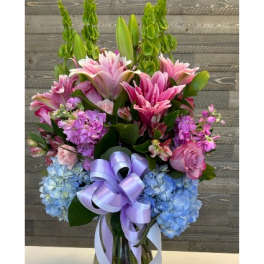 Pink lilies and blue hydrangeas in a glass vase with a lavender ribbon