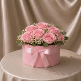 Pink roses arranged in a round pink box with a satin bow