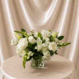 White floral arrangement in a clear glass vase on a draped table