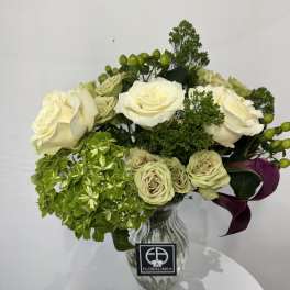 Cream roses and green hydrangea in a glass vase with purple calla lilies