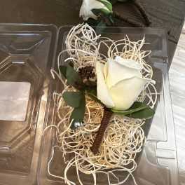 White rose boutonnieres in clear plastic packaging with straw filler.