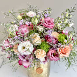 Mixed bouquet of pink and peach roses and white lisianthus in a gold cylinder vase