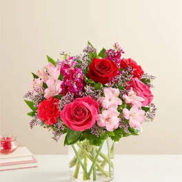 Bouquet of red and pink roses with pale pink flowers in a clear glass vase