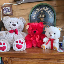 Three teddy bears with red ribbons sit on a wooden mantel.