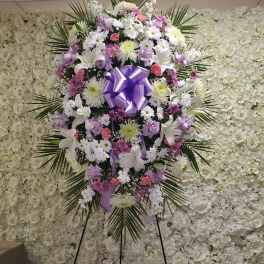 Tall standing spray of white, lavender, and pink flowers with a large lavender bow on an easel.