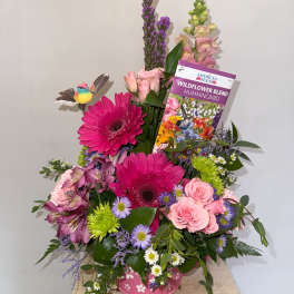 Mixed bouquet with pink gerbera daisies, roses, and purple flowers in a pink container