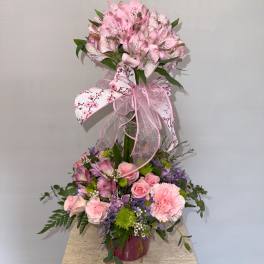Pink floral arrangement with a butterfly topper and ribbon in a vase