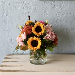 Bouquet of sunflowers and pink flowers in a clear glass vase