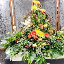 Large floral spray with lilies and bright daisy blooms in a wicker frame
