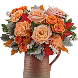 Orange and peach roses with carnations in a brown pitcher vase