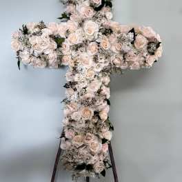 Cross-shaped floral arrangement of pale roses and white blooms on a stand