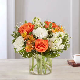 Orange roses and white flowers arranged in a clear glass vase