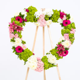 Heart-shaped floral wreath on a wooden easel with pink, white, and green flowers