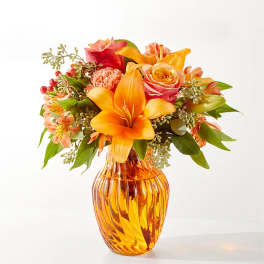 Orange and pink mixed bouquet in an amber glass vase