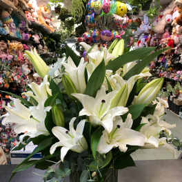 White lilies arranged in a clear glass vase with greenery