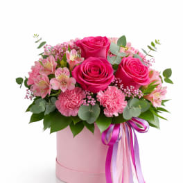 Pink roses and carnations in a pink hatbox with ribbon tails