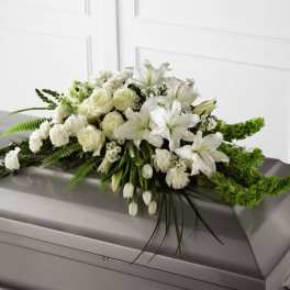 White lilies, roses, and carnations casket spray with green accents on a silver casket