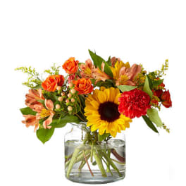 Bouquet of sunflowers, orange roses, and red carnations in a glass vase