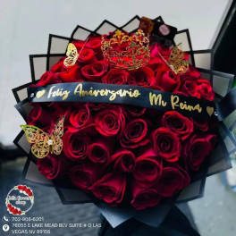 Round bouquet of red roses wrapped in black paper with a gold crown and butterflies on top.