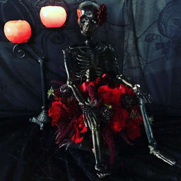 Skeleton figure surrounded by red roses and candles on a dark background