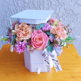 Pink and peach flowers arranged in a white graduation box with a cap lid