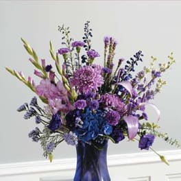 Tall purple and blue mixed flower arrangement in a blue vase with ribbon accents