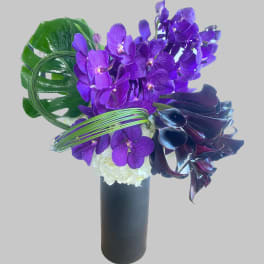 Purple orchids and white flowers in a black vase with large green leaves