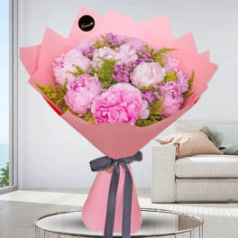 Pink bouquet of peonies wrapped in pink paper with a dark ribbon