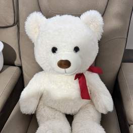 White teddy bear with a red ribbon sitting on a chair
