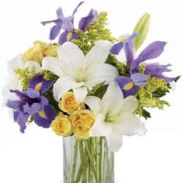 Bouquet of white lilies, purple irises, and yellow roses in a clear glass vase
