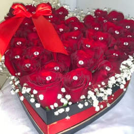 Heart-shaped box filled with red roses and a red ribbon bow