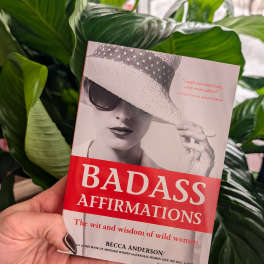 Hand holding a book in front of large green plant leaves