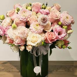 Pink and cream rose bouquet in a dark green vase with a sheer ribbon