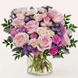 Pink roses and purple daisies arranged in a clear glass vase