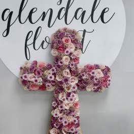 Cross-shaped floral arrangement in pink and purple roses with small daisy-like blooms