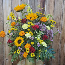 Mixed bouquet of sunflowers, roses, and marigolds in a gold vase