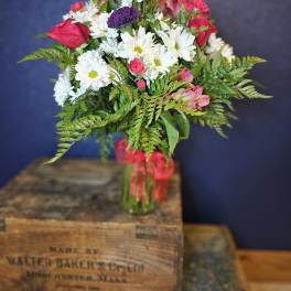Bouquet of white daisies, pink roses, and purple blooms in a glass vase