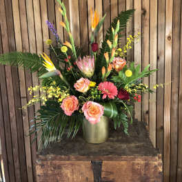 Tall tropical bouquet with orange and pink flowers in a gold vase