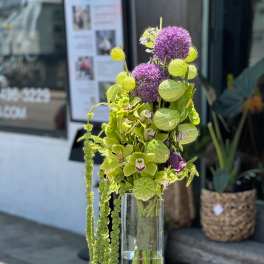 Tall vase arrangement with green orchids and purple allium