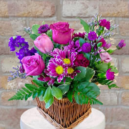 Pink and purple mixed flower arrangement in a rectangular wicker basket