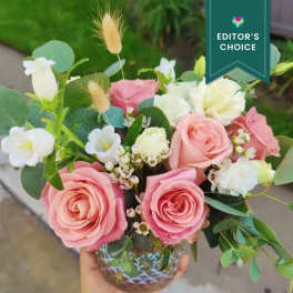 Pink and white roses arranged in a glass vase with greenery.