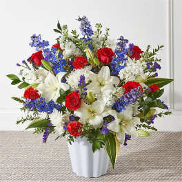 Mixed bouquet of red roses, white lilies, and blue flowers in a white vase